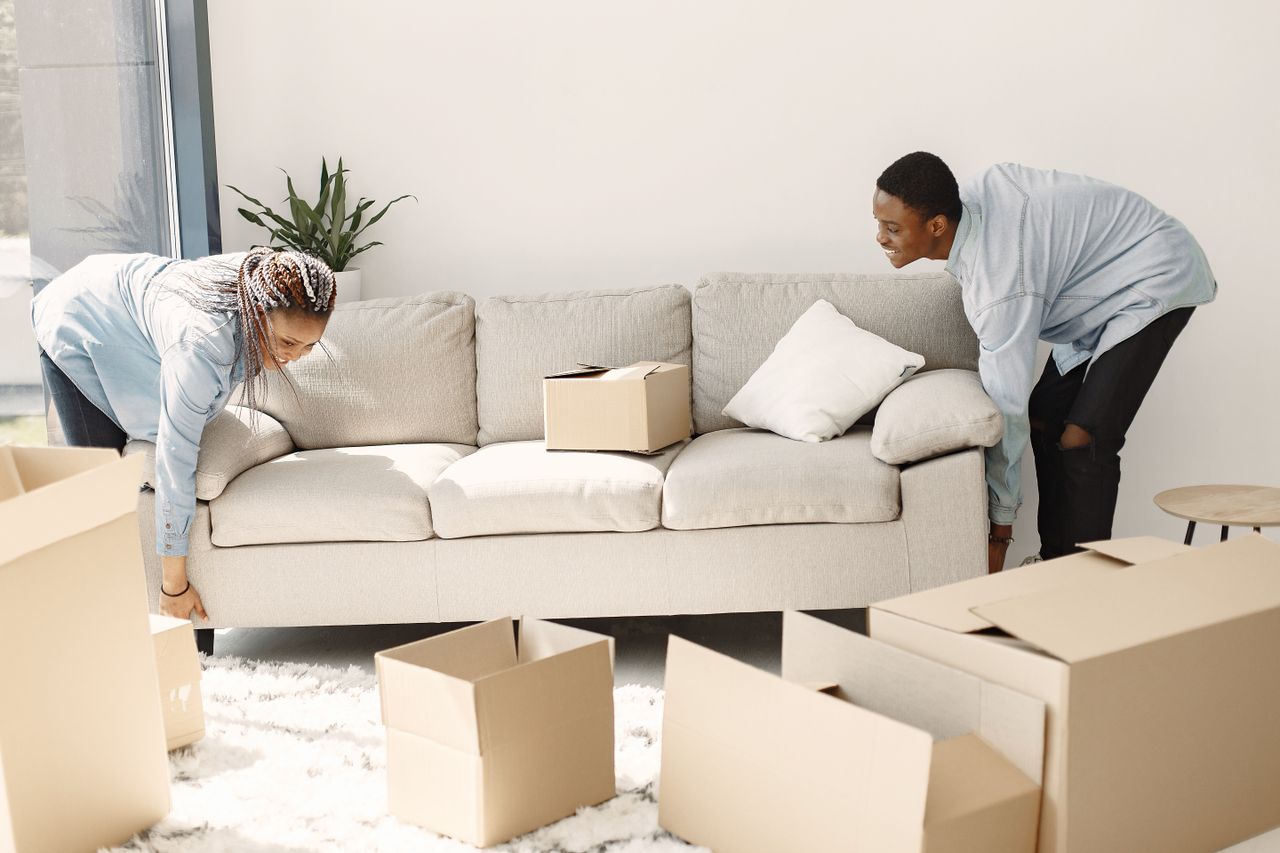 team-01 Happy couple arranging a sofa in their new home, with moving boxes all around.